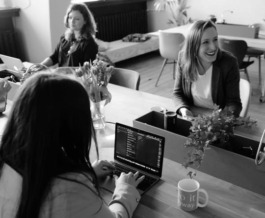 Three women working on their laptops around a dining table.